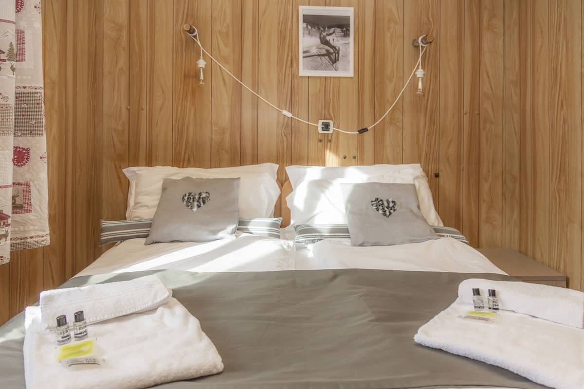 A neatly made bed with pillows, a bedside table with a lamp, and a wooden wall with a framed picture.