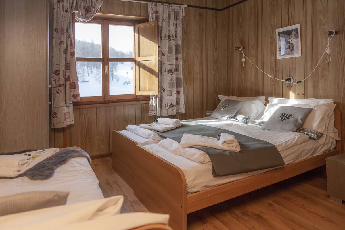 A wooden-paneled bedroom with a bed, a window with curtains, and a picture on the wall.