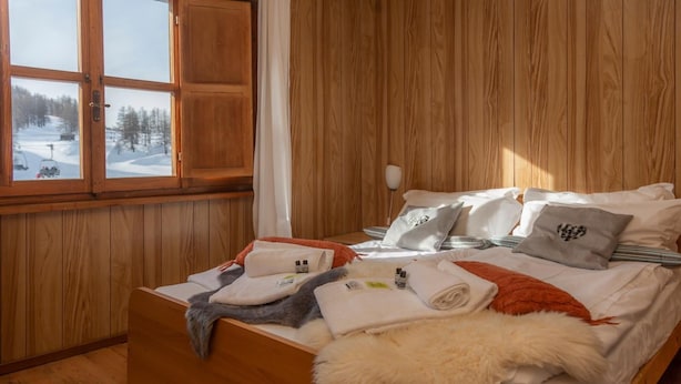 Una habitación con paneles de madera, una cama, almohadas y un ventanal con vistas a un paisaje nevado.