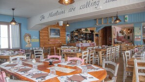 Un restaurante con mesas y sillas de madera, una zona de bar y un mural en la pared.