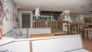 Zona de bar con mostrador, taburetes y área de estar con sofá y sillas.