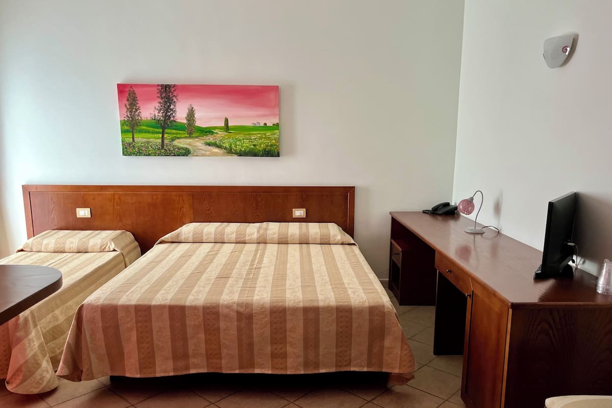 A hotel room with two beds, a desk, a chair, a TV, and a painting of a landscape.