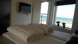 Una camera da letto con un letto, una TV a muro e una finestra vista spiaggia.
