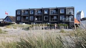 Un moderno edificio a più piani con balconi, situato su una spiaggia sabbiosa con vegetazione sullo sfondo.