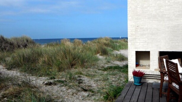 Vista sulla spiaggia con un pontile in legno e un edificio bianco con un piccolo ingresso.