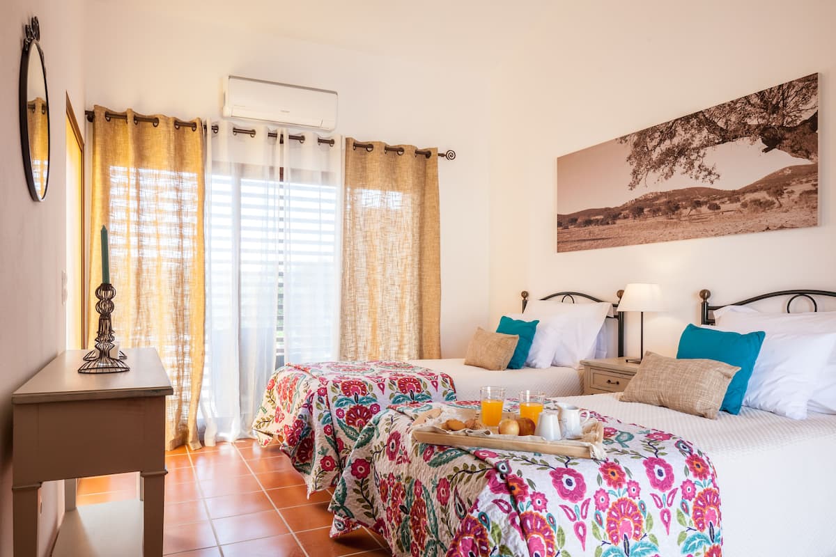 A hotel room with two beds, a small table with a tray of breakfast, a mirror, and a painting on the wall.