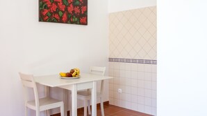 A small dining area with a white table and chairs, a painting of red flowers on the wall, and a tiled backsplash. - Monte da Esperança (Arronches)