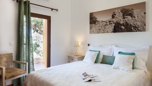 A neatly made bed with white bedding and green pillows, a bedside table with a lamp, a chair, and a large framed picture on the wall. - Monte da Esperança (Arronches)