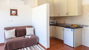 A compact kitchenette with a microwave, sink, and small refrigerator. A brown sofa with pillows is positioned against the wall, and a striped rug is on the floor. - Monte da Esperança (Arronches)