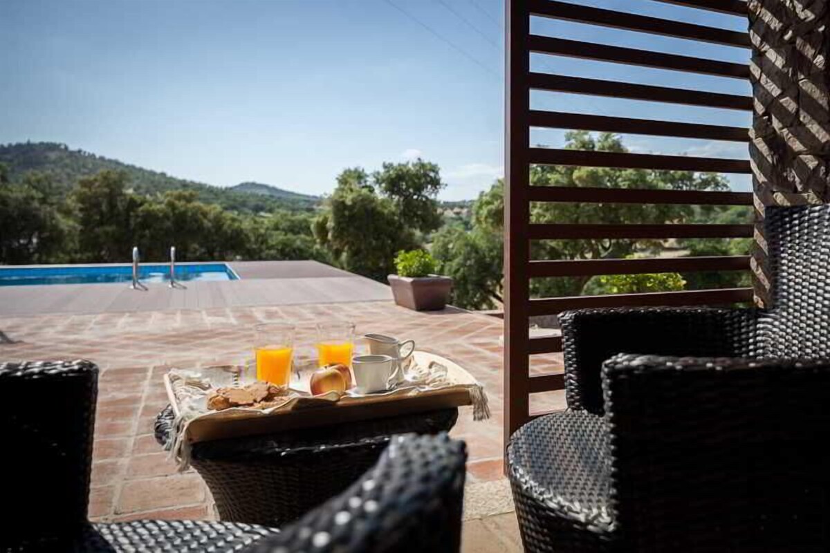 A patio with wicker furniture, a breakfast tray, and a view of a swimming pool and hills.