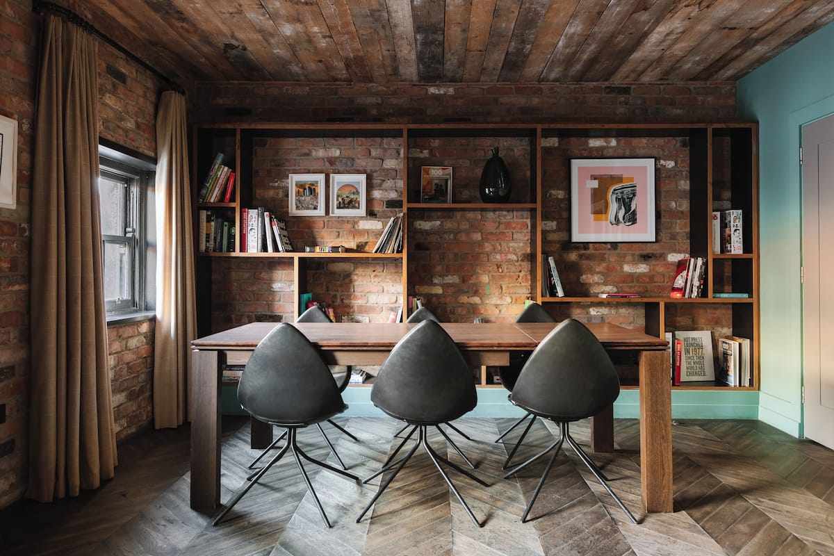 A rustic dining area with a brick wall, wooden table, and modern chairs.