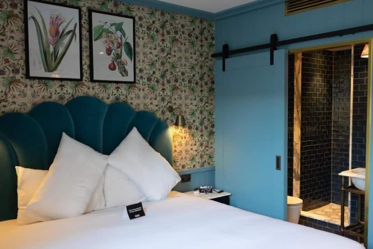 A hotel room with a teal headboard, floral wallpaper, and a bed with white linens.