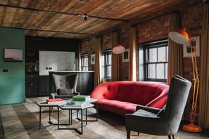 Un salon moderne avec un canapé rouge, un fauteuil gris et une table basse. On y trouve un mur en briques et une fenêtre avec des rideaux.
