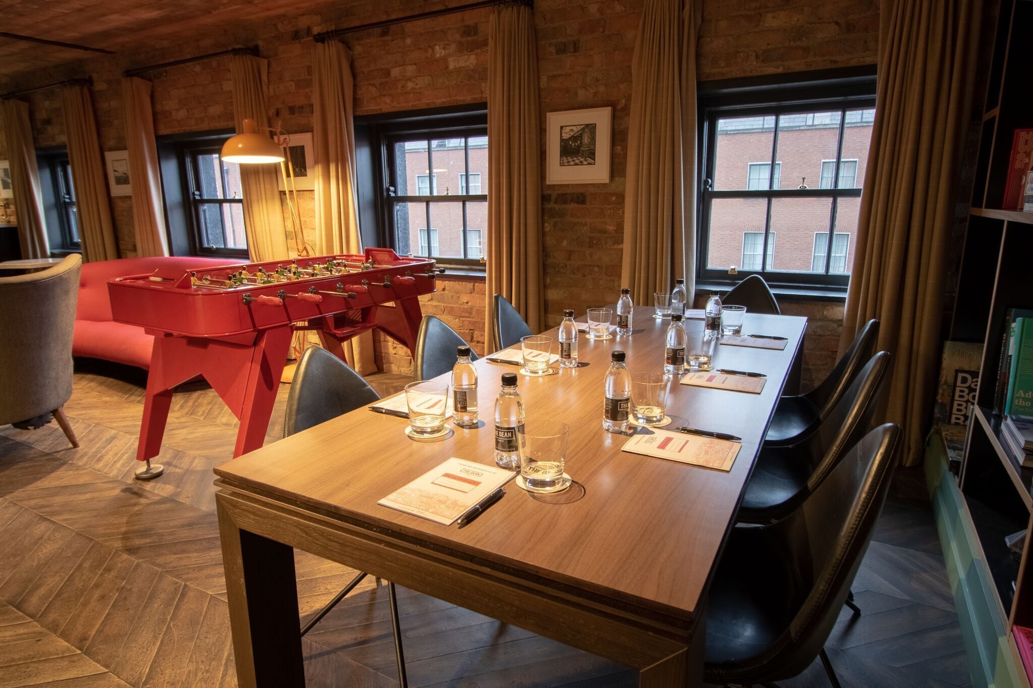 A conference room with a long table set for a meeting, a foosball table, and a sofa in the background.