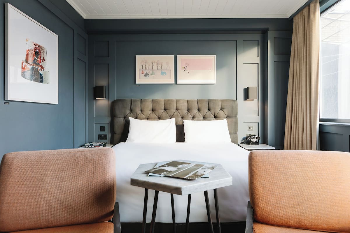 A hotel room with a large bed, two armchairs, a small table, and artwork on the walls.