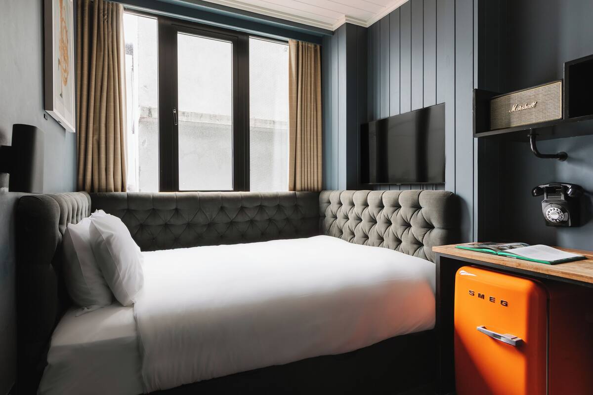 A hotel room with a bed, a television, a minibar, and a window with curtains.