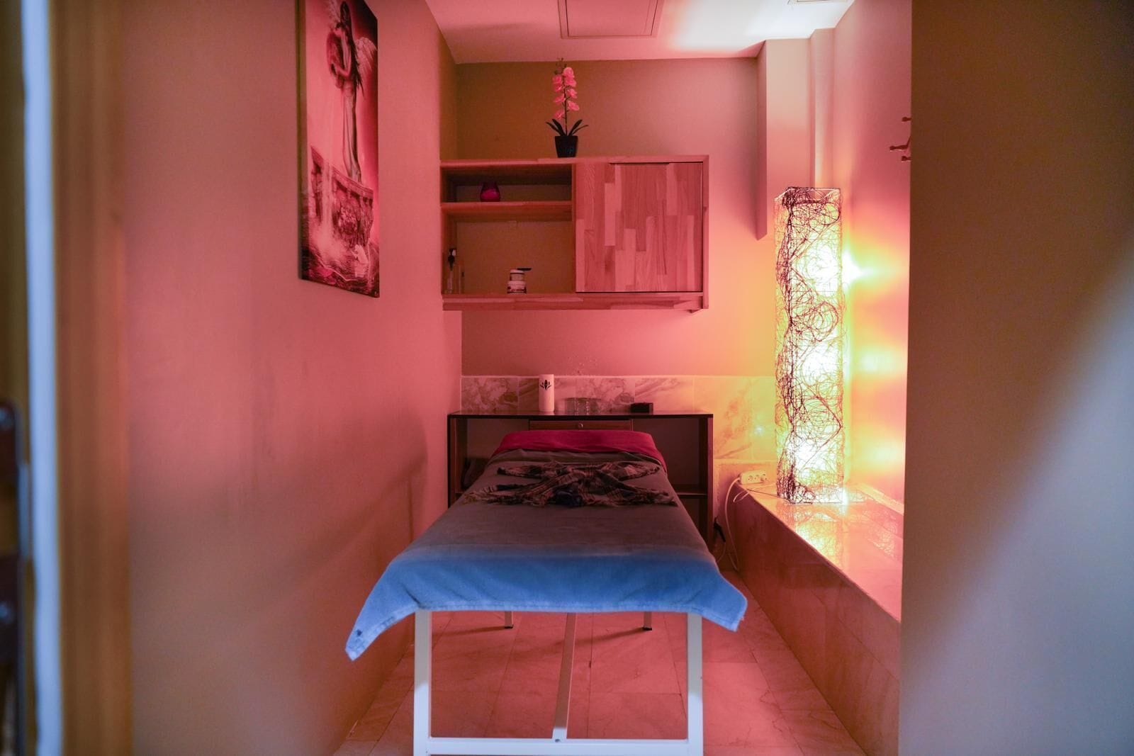 Un pasillo estrecho con una cama al final, un armario de madera encima y una lámpara fijada a la pared.