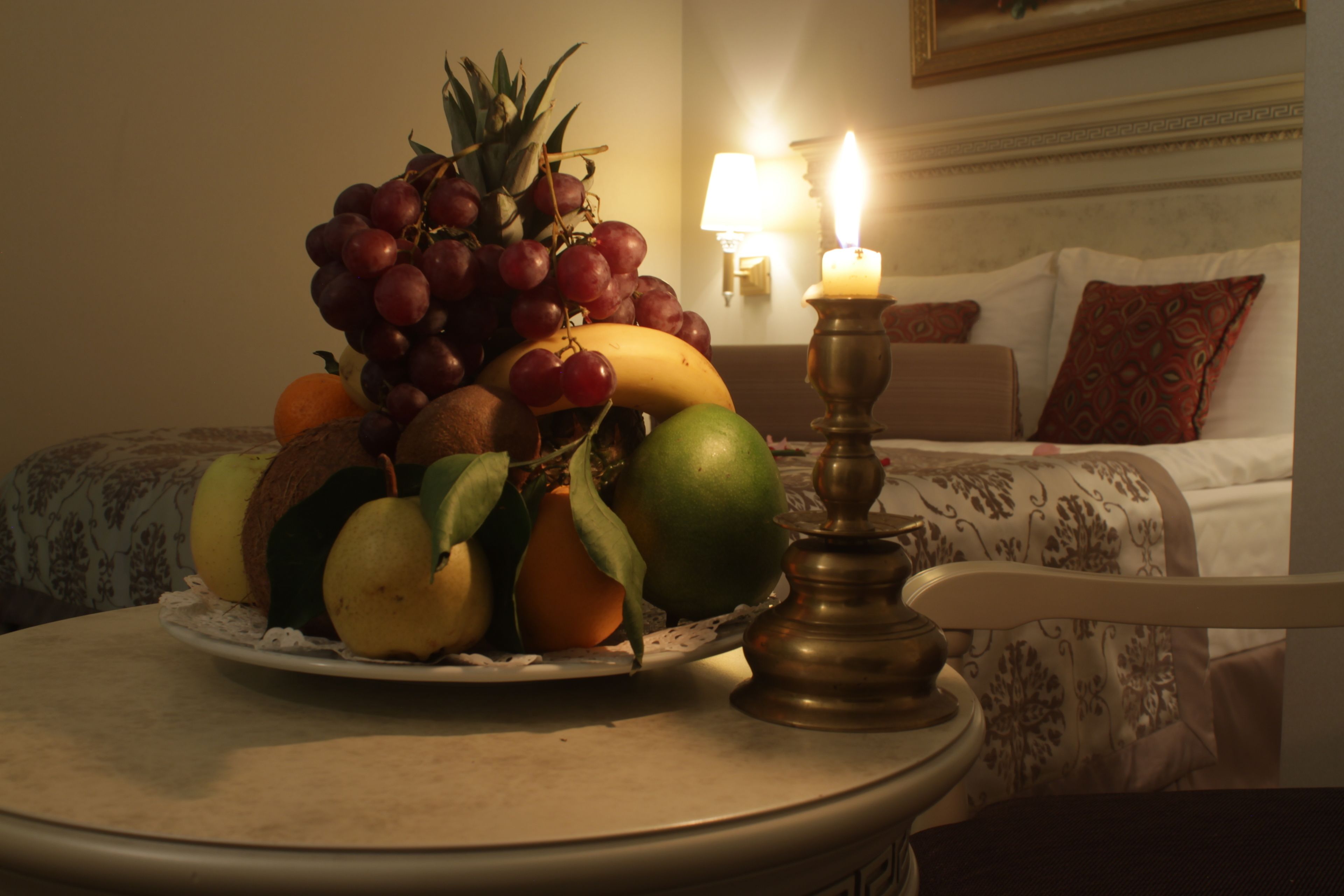 Une assiette de fruits est posée sur une table dans une chambre d’hôtel, avec un lit et une lampe en arrière-plan.