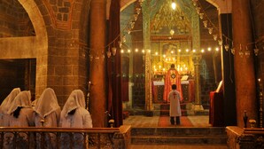 An interior view of a church with a central altar, stone columns, and a group of people in white robes. - Demir Hotel (Diyarbakir)