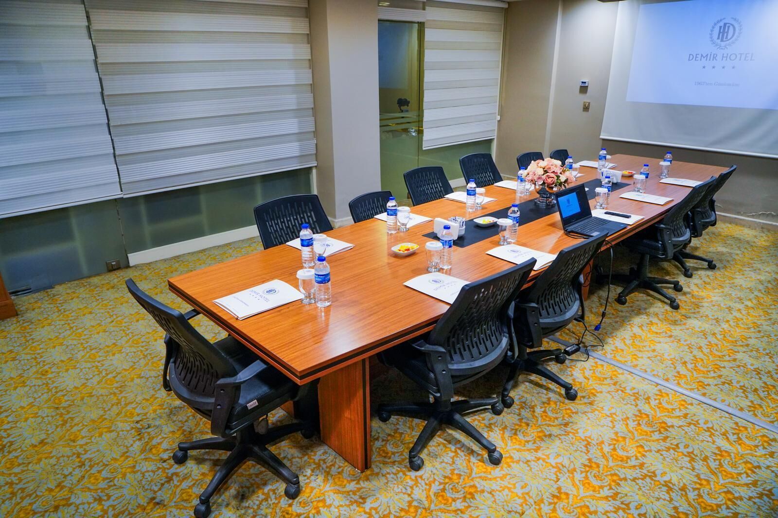 A conference room with a long table, chairs, water bottles, and a laptop.