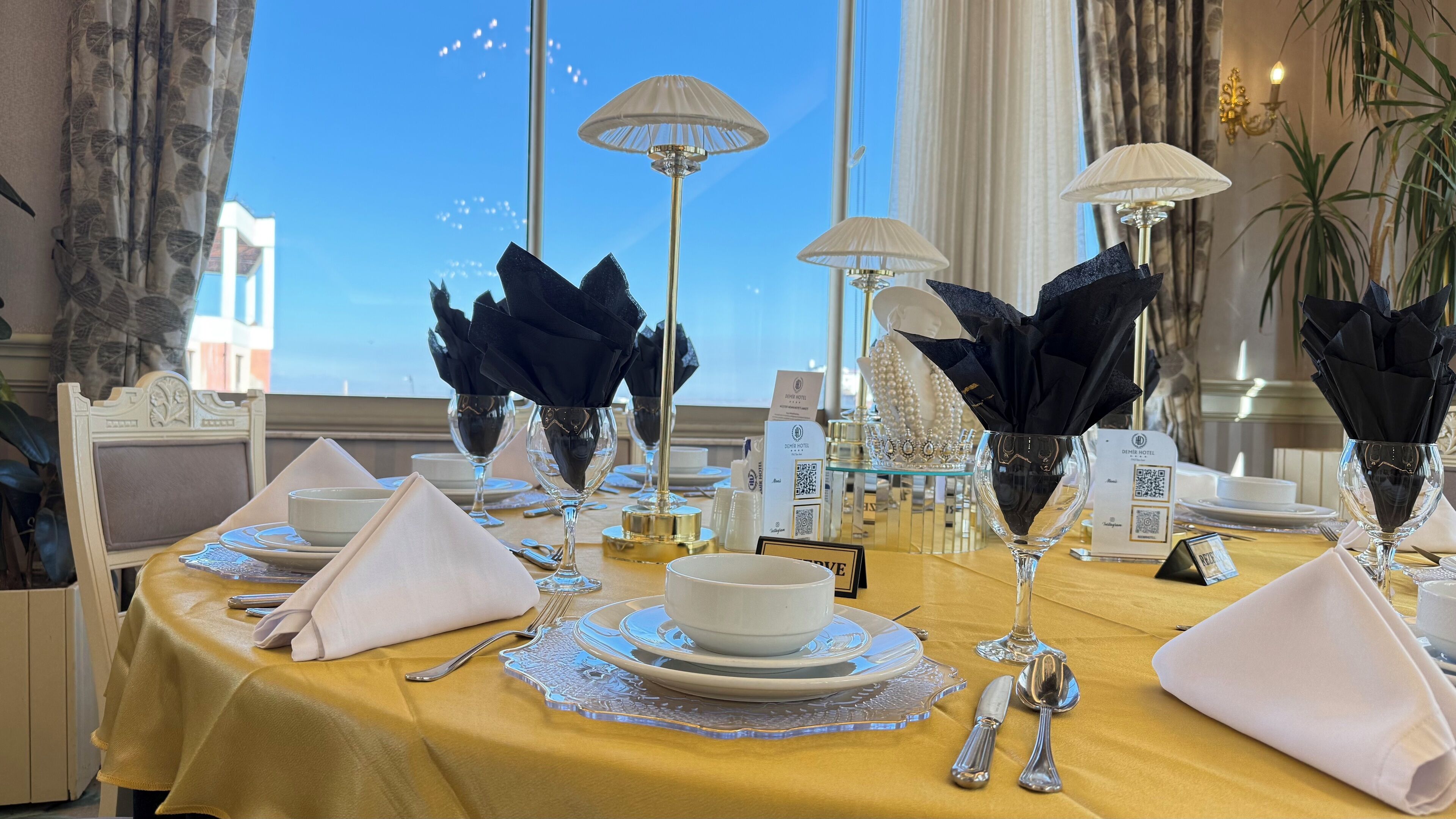 Una mesa dispuesta para comer, con cristalería transparente, servilletas dobladas y un mantel amarillo.
