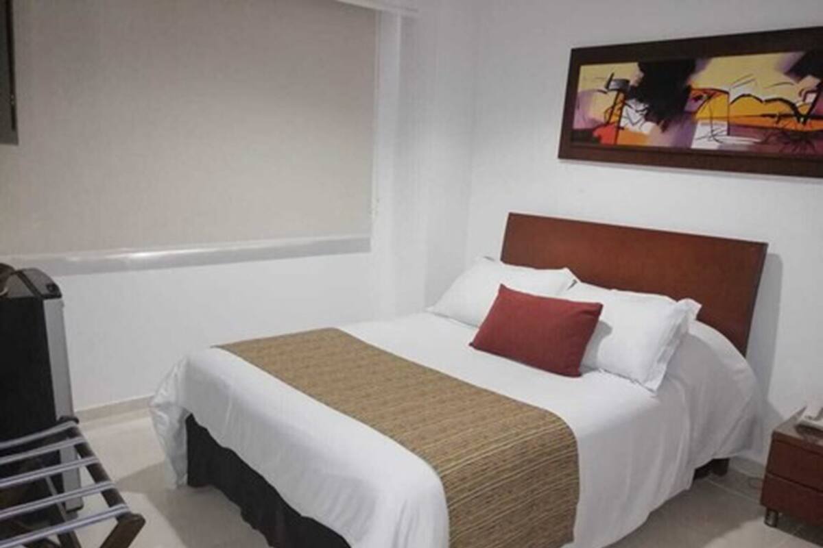 Una habitación de hotel con cama, mesita de noche, un cuadro en la pared y una ventana.