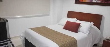 A hotel room with a bed, a nightstand, a painting on the wall, and a window.