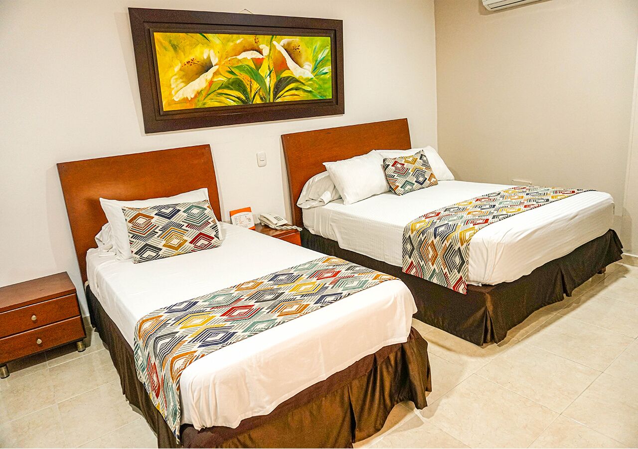 A hotel room with two beds, each with a patterned bedspread and matching pillows, a wooden headboard, and a wall-mounted air conditioner.