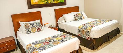 A hotel room with two beds, each with a patterned bedspread and matching pillows, a wooden headboard, and a wall-mounted air conditioner.