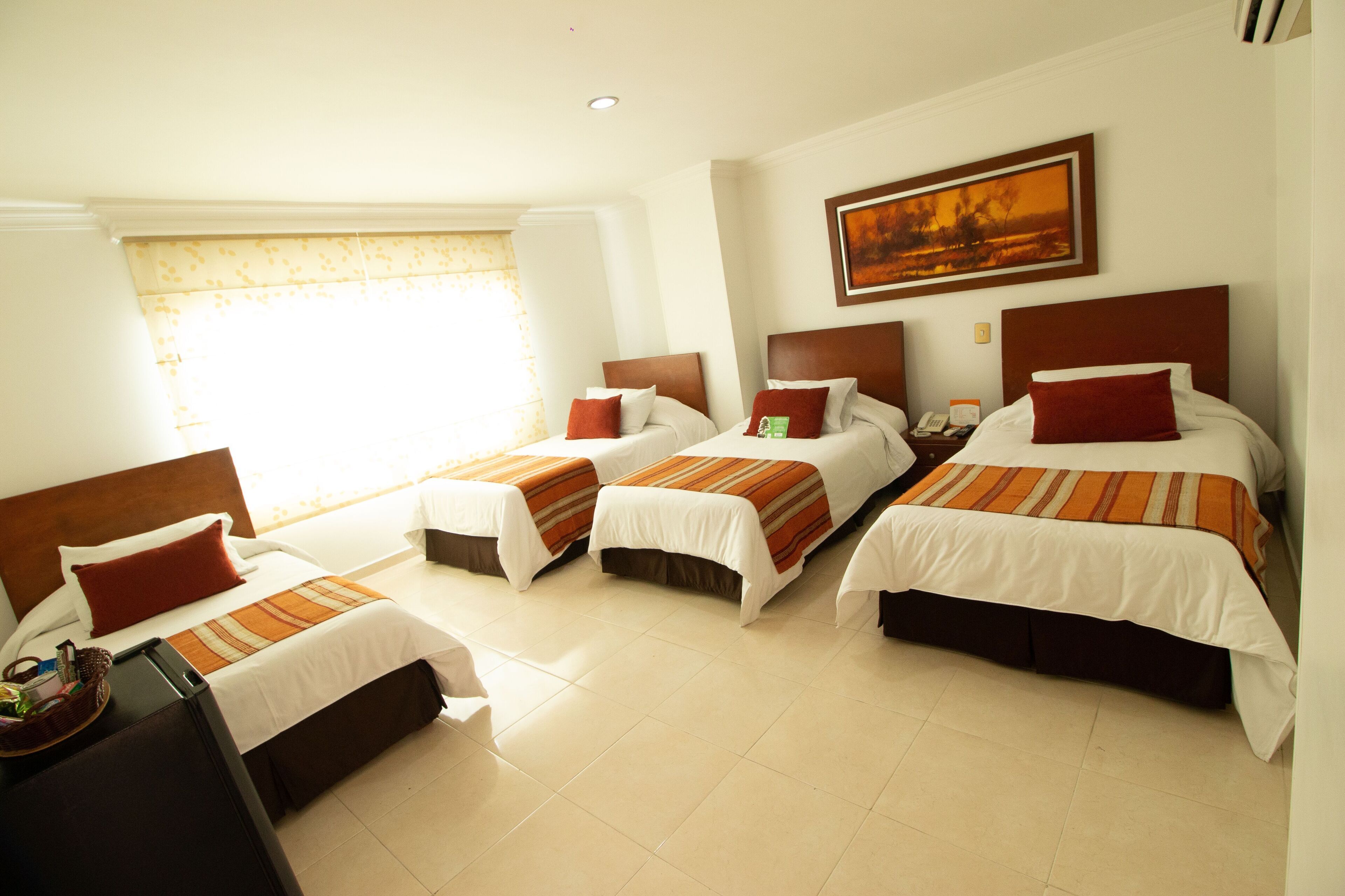 Habitación de hotel con cuatro camas individuales, un escritorio y una ventana con cortinas.
