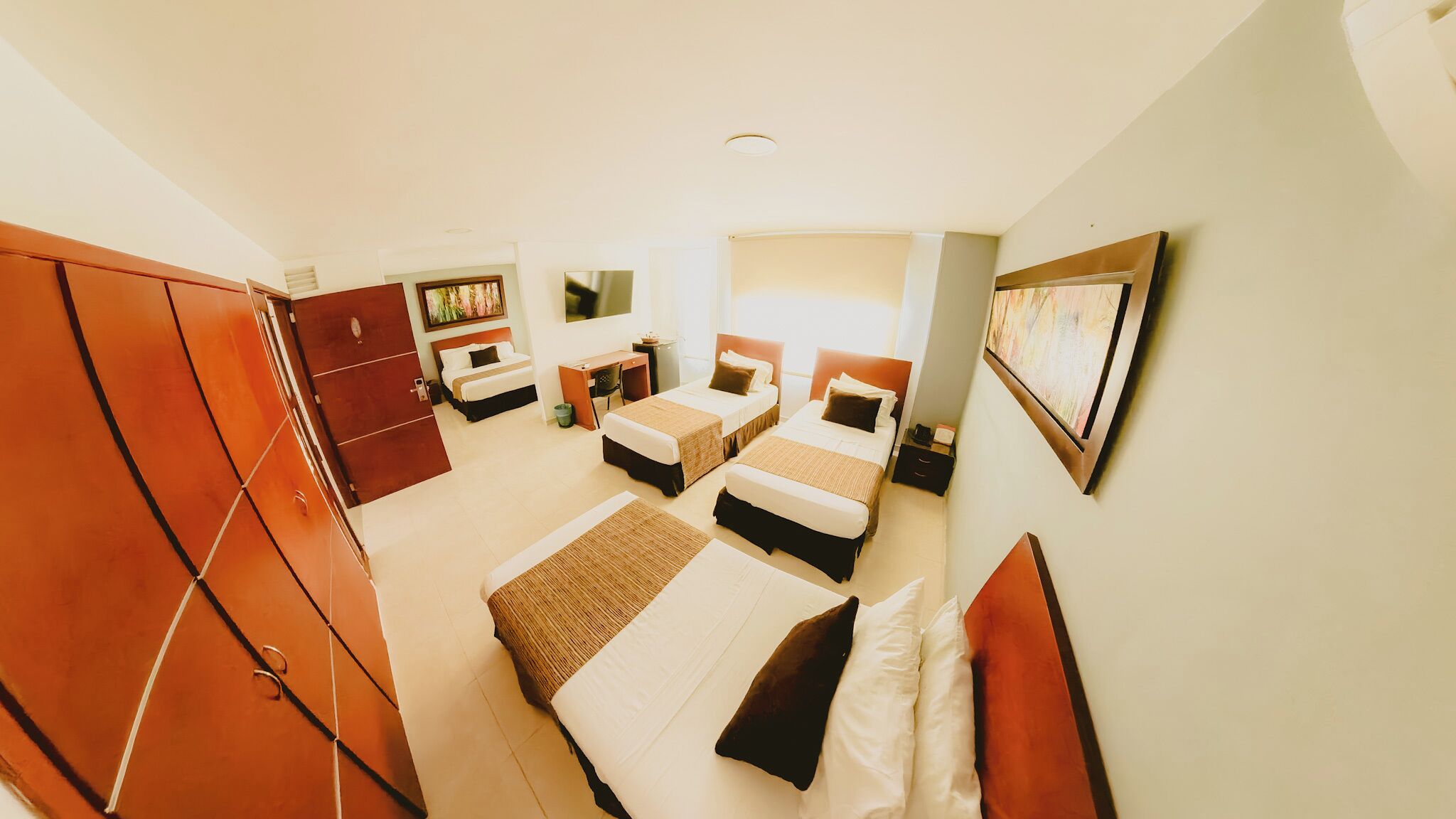 A hotel room with two beds, a desk, a wardrobe, and a painting on the wall.