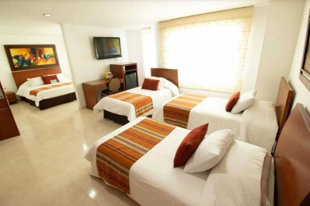 Una habitación de hotel con tres camas, un escritorio, un televisor y obras de arte en la pared.