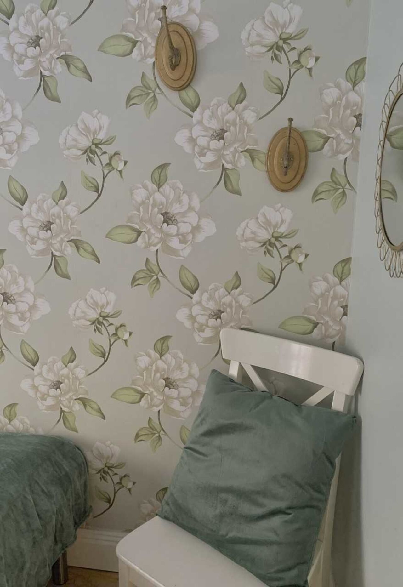 A bedroom with a floral wallpaper, a white bed, and a green pillow.