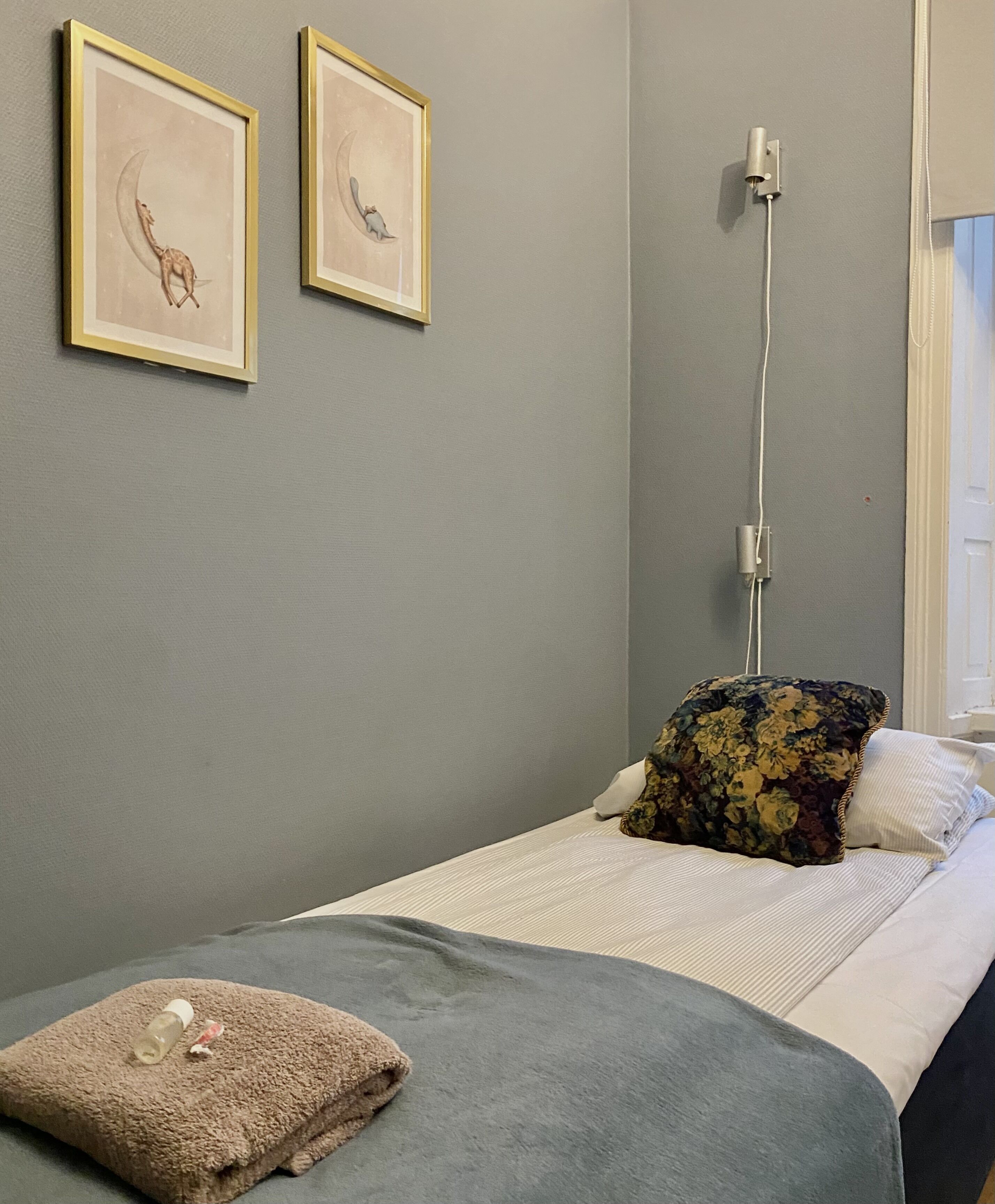Un dormitorio con cama, almohada, manta y dos cuadros en la pared.