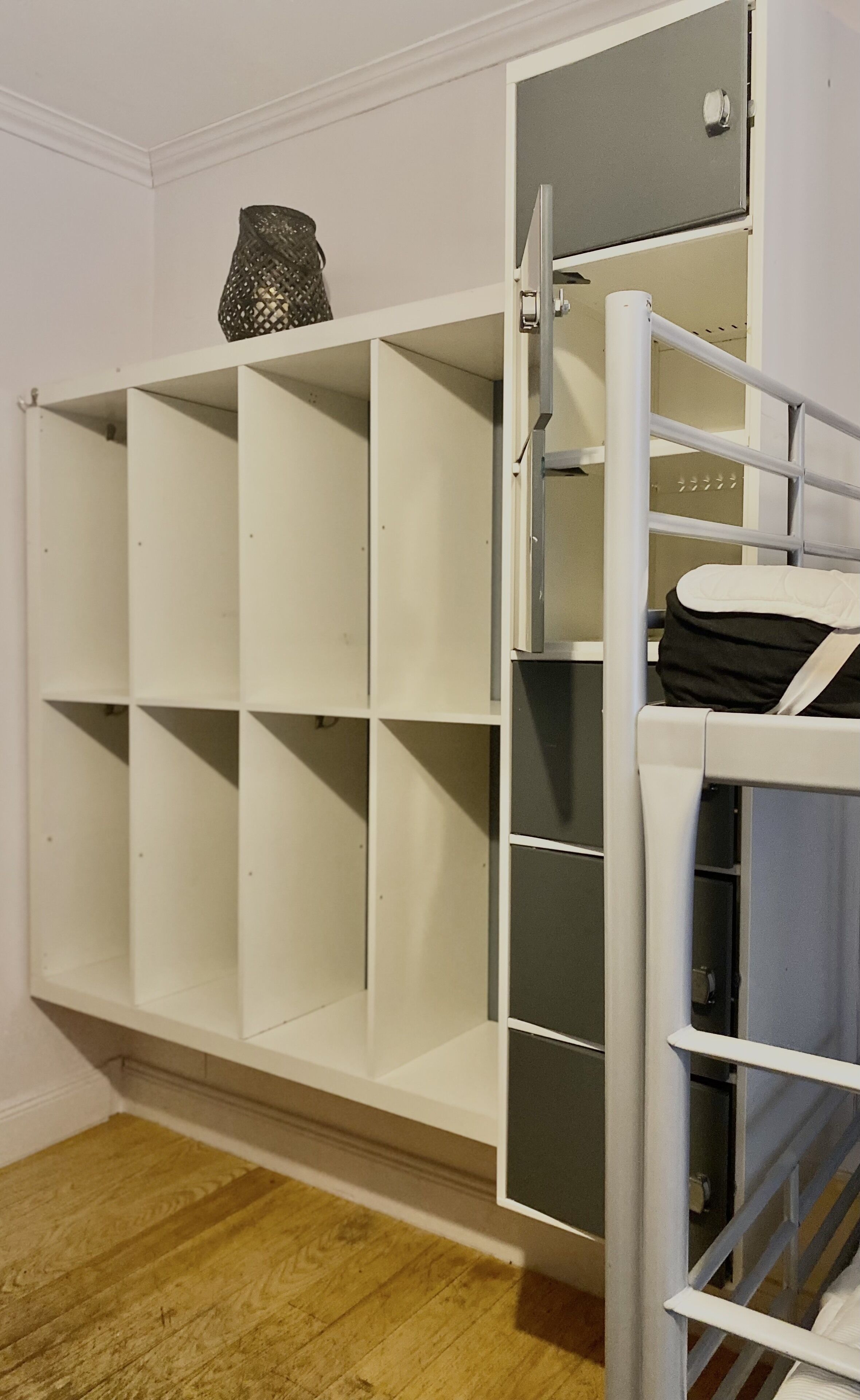 Un meuble de rangement blanc doté de plusieurs compartiments, une petite étagère ornée d’un objet décoratif et une échelle en métal pour accéder aux étagères les plus hautes.
