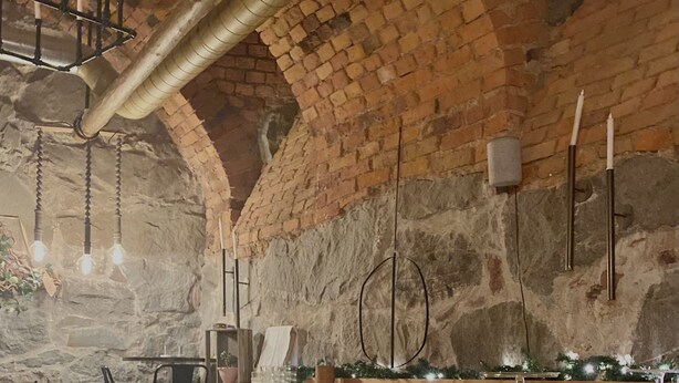 A rustic interior with exposed brick walls, wooden tables and chairs, and hanging light fixtures. - Lilla Brunn - Hostel (Stockholm)