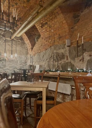 A rustic interior with exposed brick walls, wooden tables and chairs, and hanging light fixtures. - Lilla Brunn - Hostel (Stockholm)
