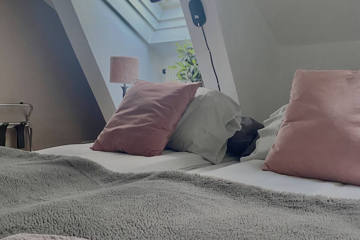 Un dormitorio con tragaluz, una cama con almohadas, una lámpara de noche y una toalla en el suelo.