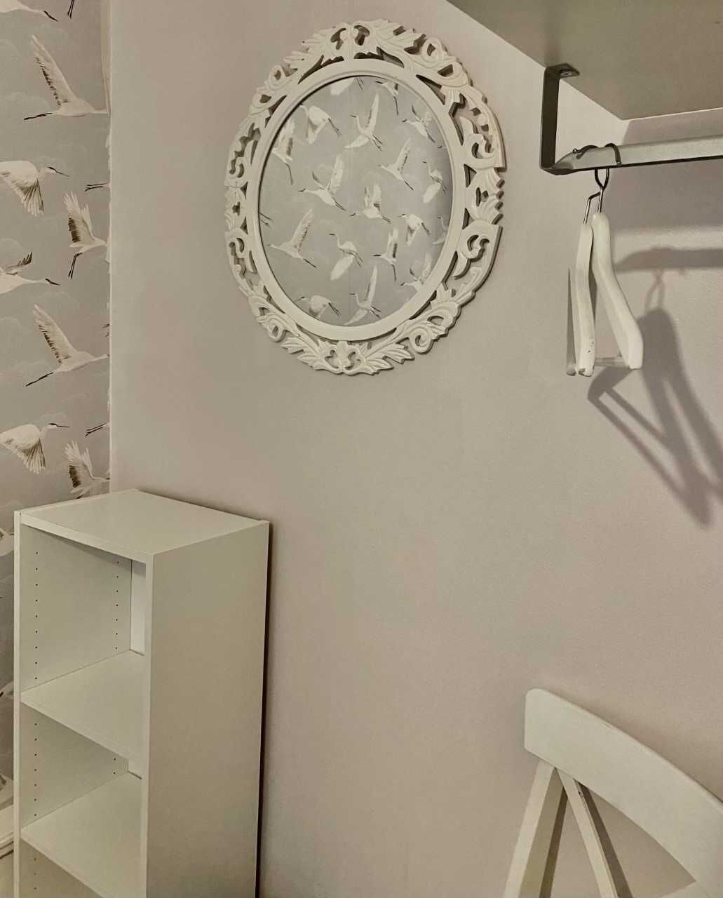 A wall with a decorative mirror and a white shelf unit.