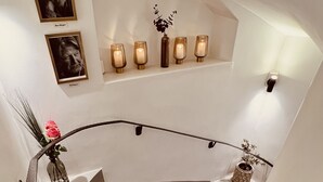 A staircase with a wooden handrail, a vase with a pink flower, and wall-mounted lights. - Lilla Brunn - Hostel (Stockholm)