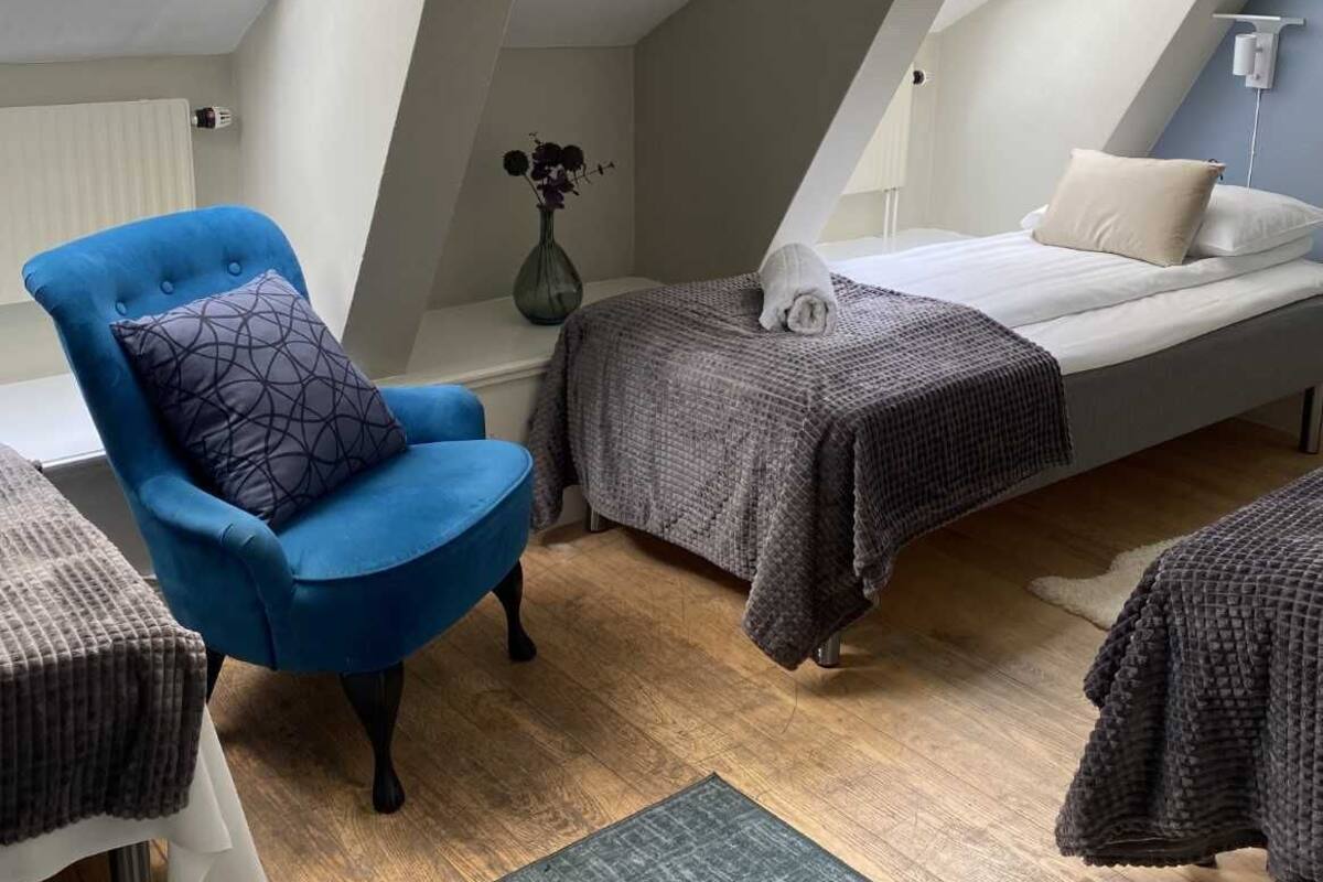 Un dormitorio pequeño y moderno con tragaluces, un sillón azul, una mesita de noche y una cama con una manta gris.