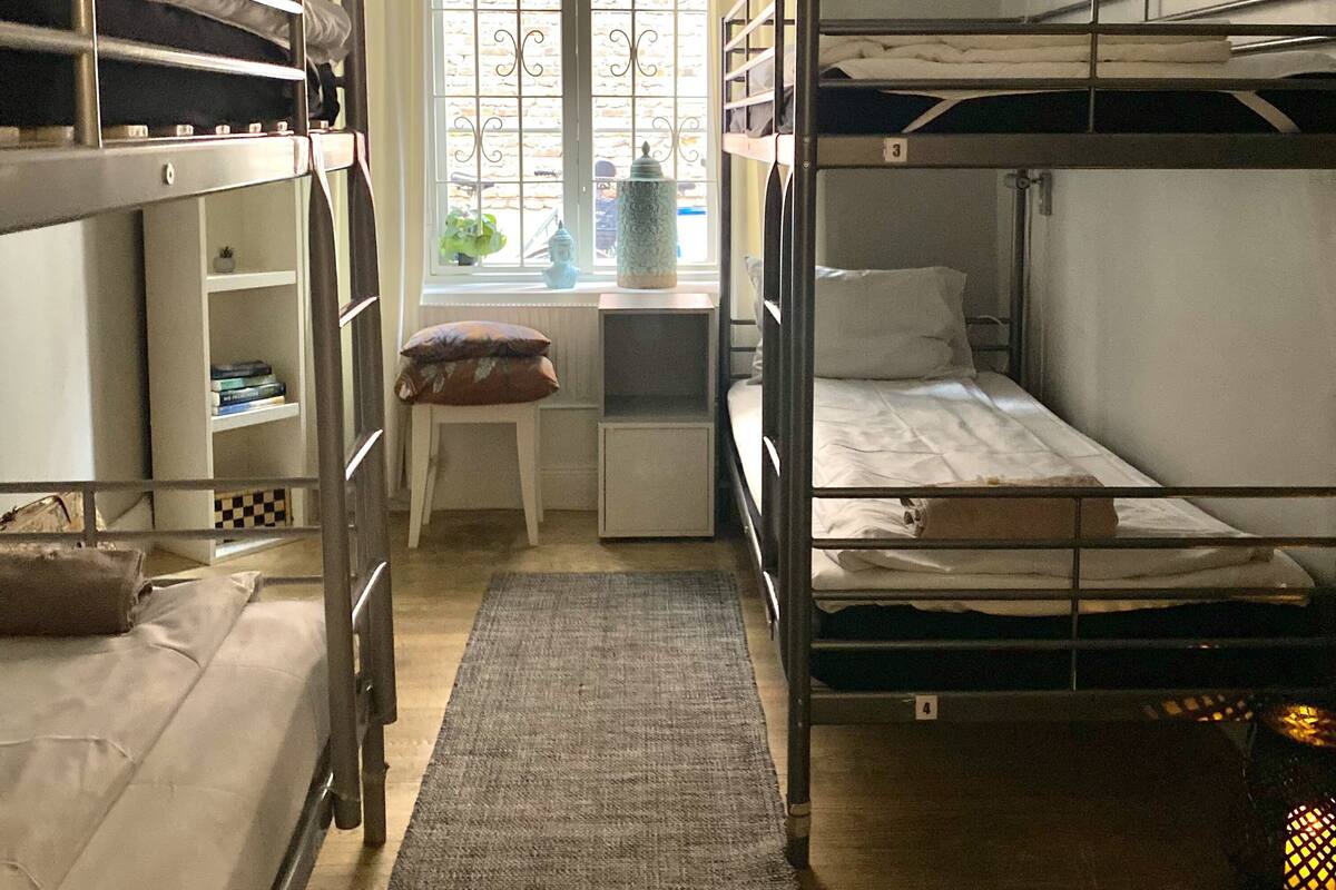 Un dormitorio con literas, un escritorio, una silla, un ventanal con cortinas y un radiador.