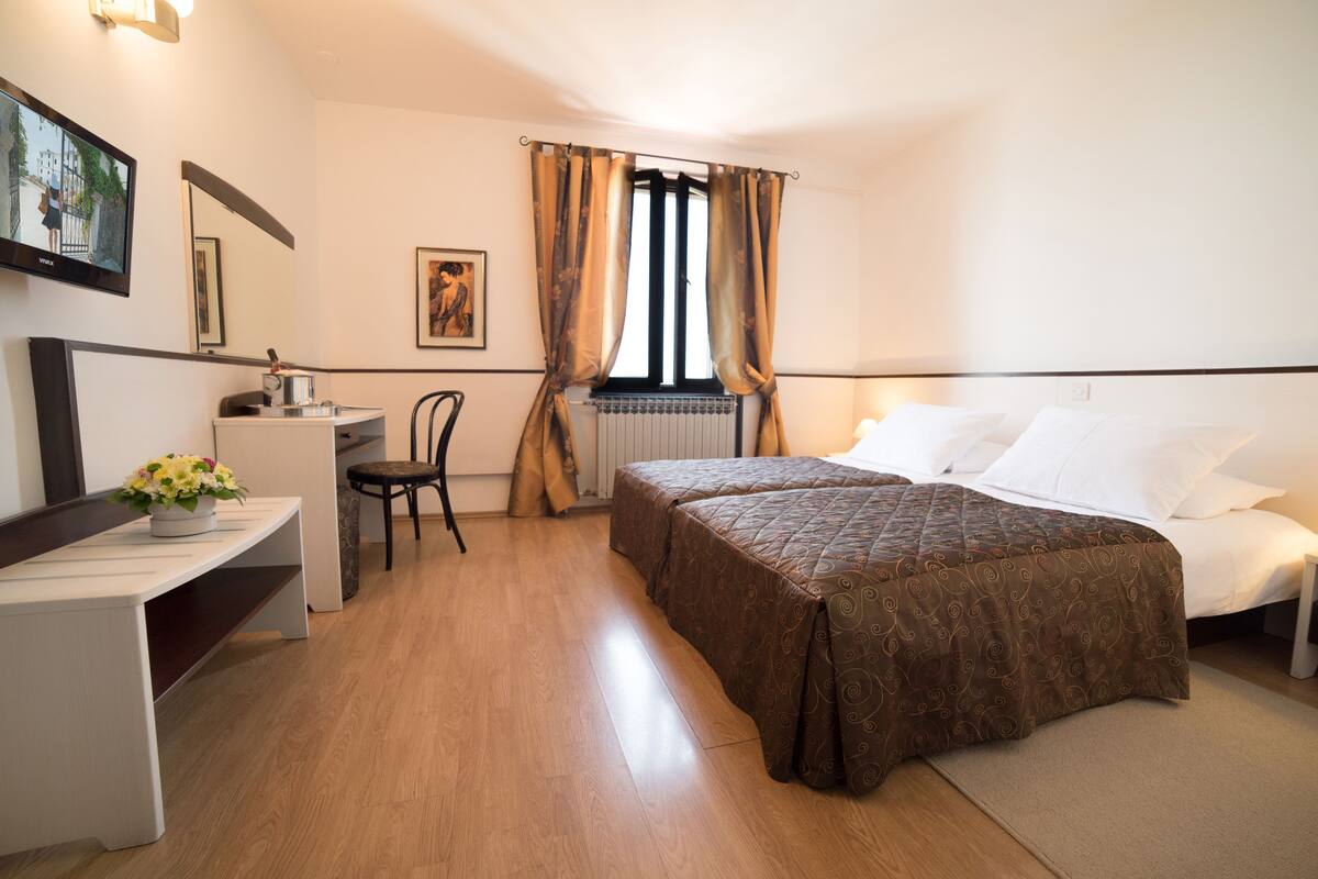 Hotellihuone, jossa on sänky, työpöytä, tuoli, patteri ja ikkuna, jossa on verhot.