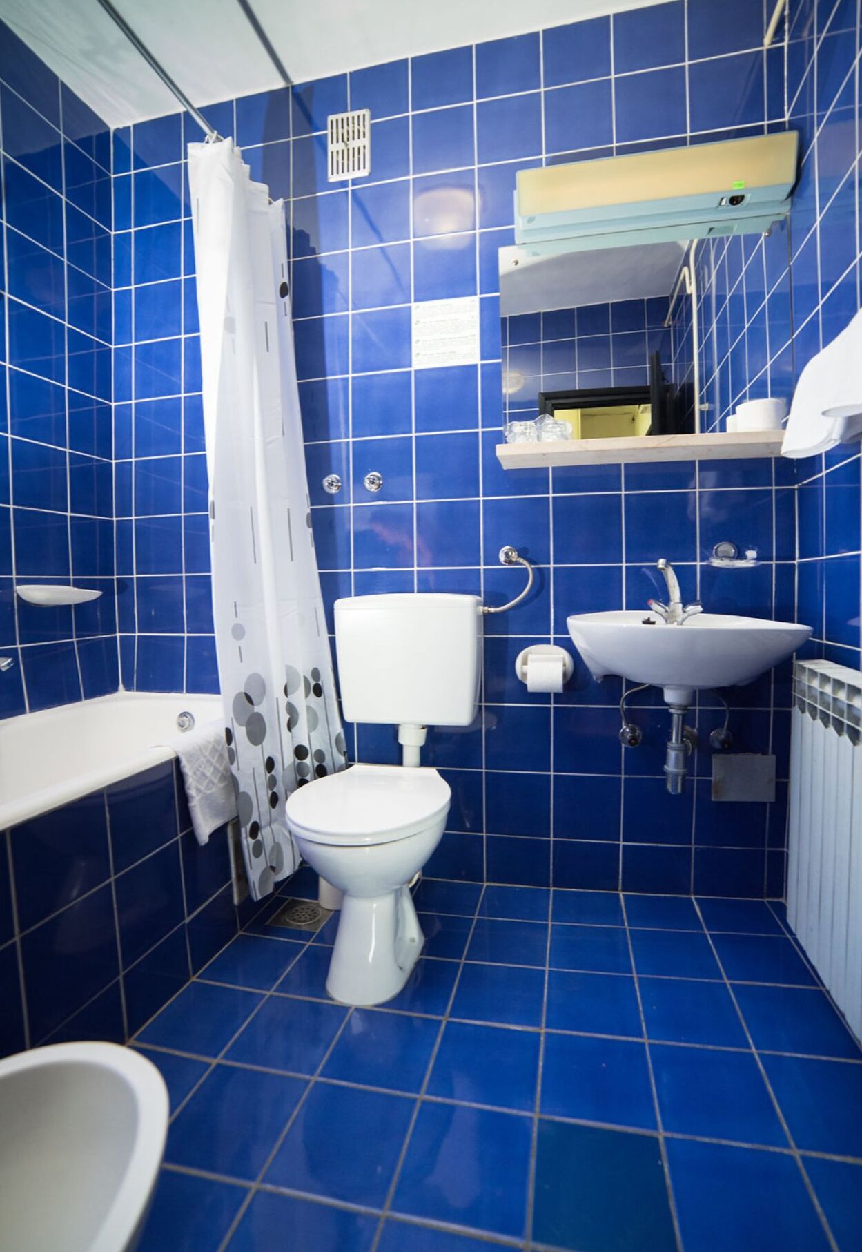 A bathroom with blue tiles, a white toilet, a sink, and a shower area.