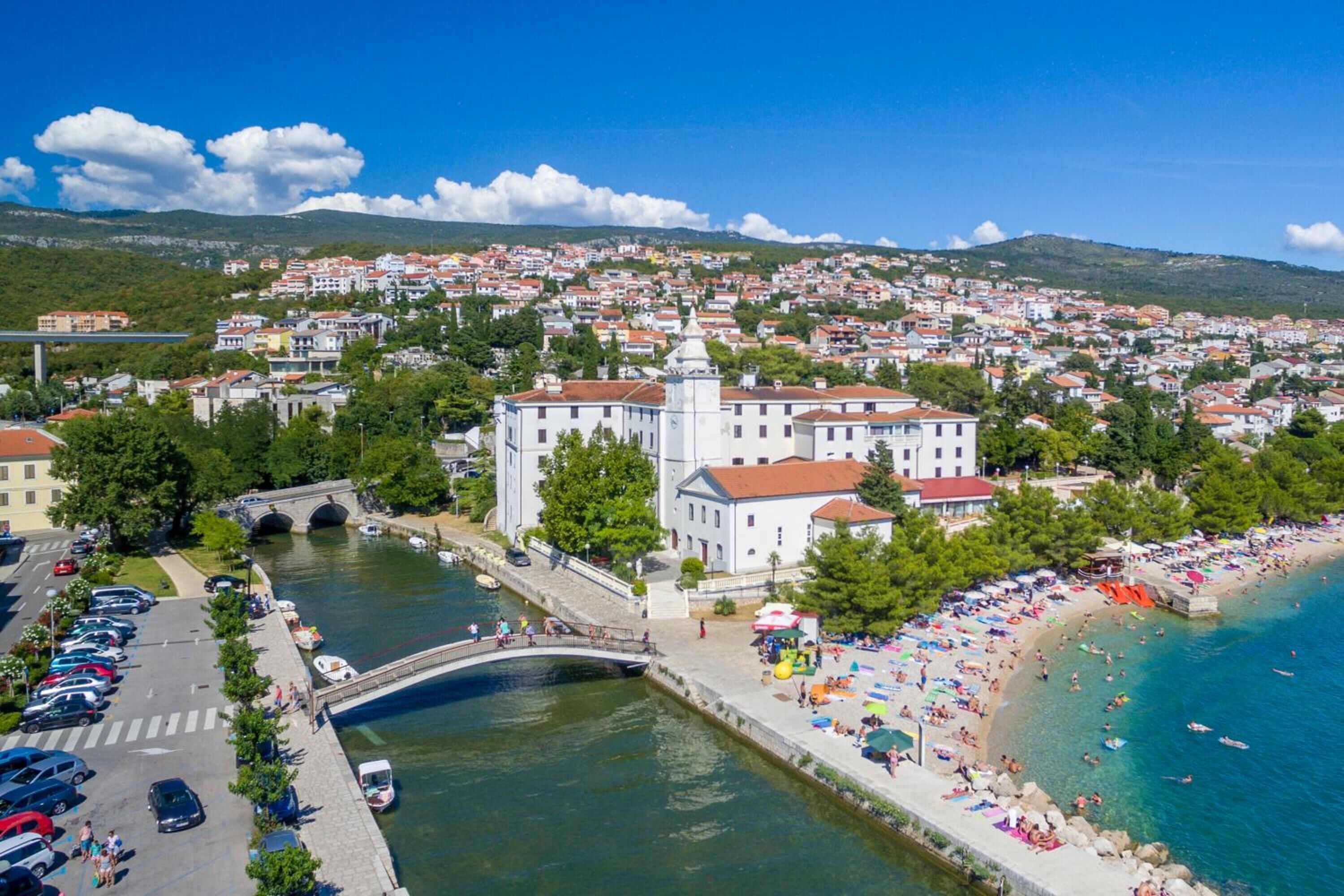 Une ville côtière qui se distingue par un imposant bâtiment blanc, un pont enjambant une rivière et une plage très fréquentée.