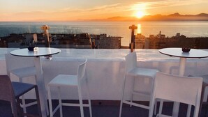 A rooftop terrace with white chairs and tables, overlooking a cityscape and the sea at sunset. - BLUESEA Arenal Tower (Llucmajor)