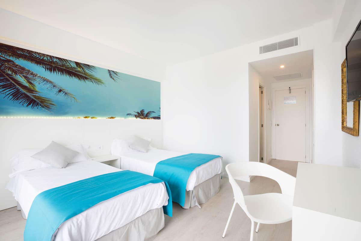 A hotel room with two beds, a desk, and a chair.
