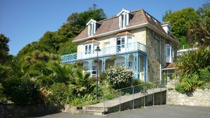 A two-story building with a balcony, surrounded by lush greenery and a stone wall.