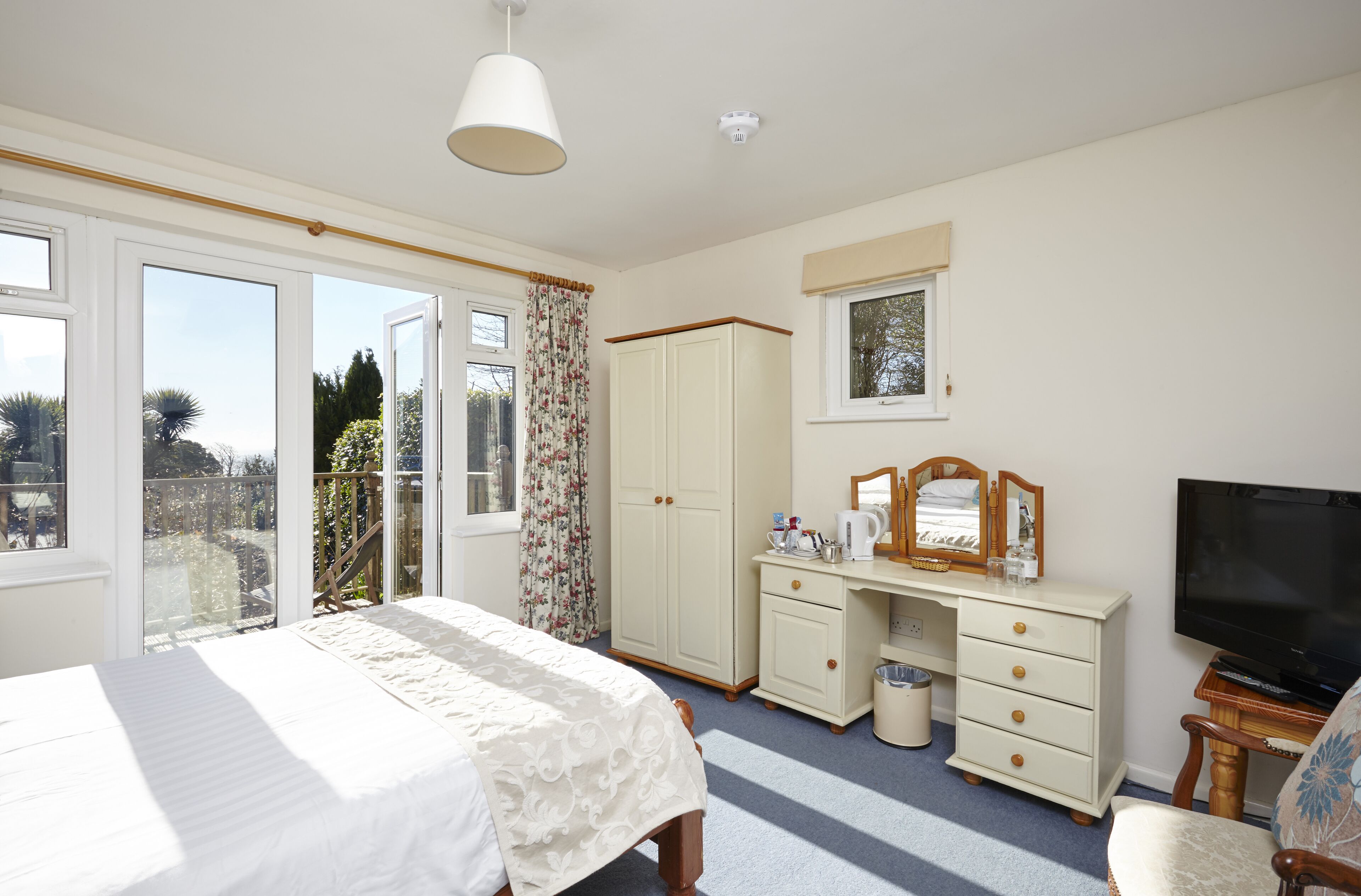 A bedroom with a bed, a dresser, a television, and a window with a view of the outdoors.