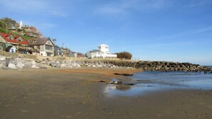 A beach with a rocky shoreline, a white building with a dome, and houses with red roofs.